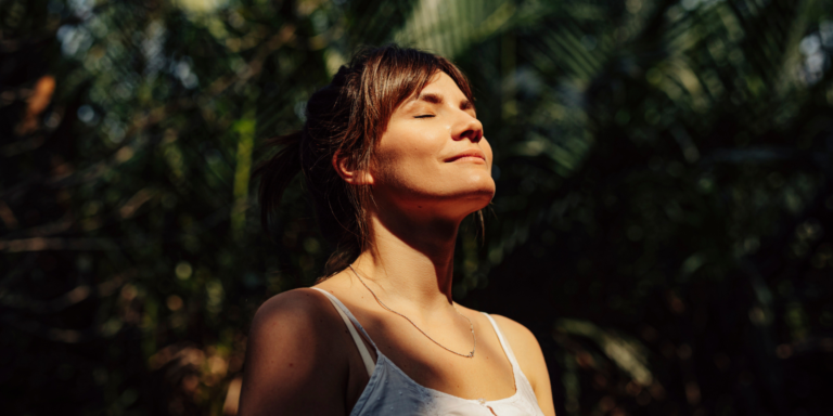 Woman stands outside enjoying the sun on her face.
