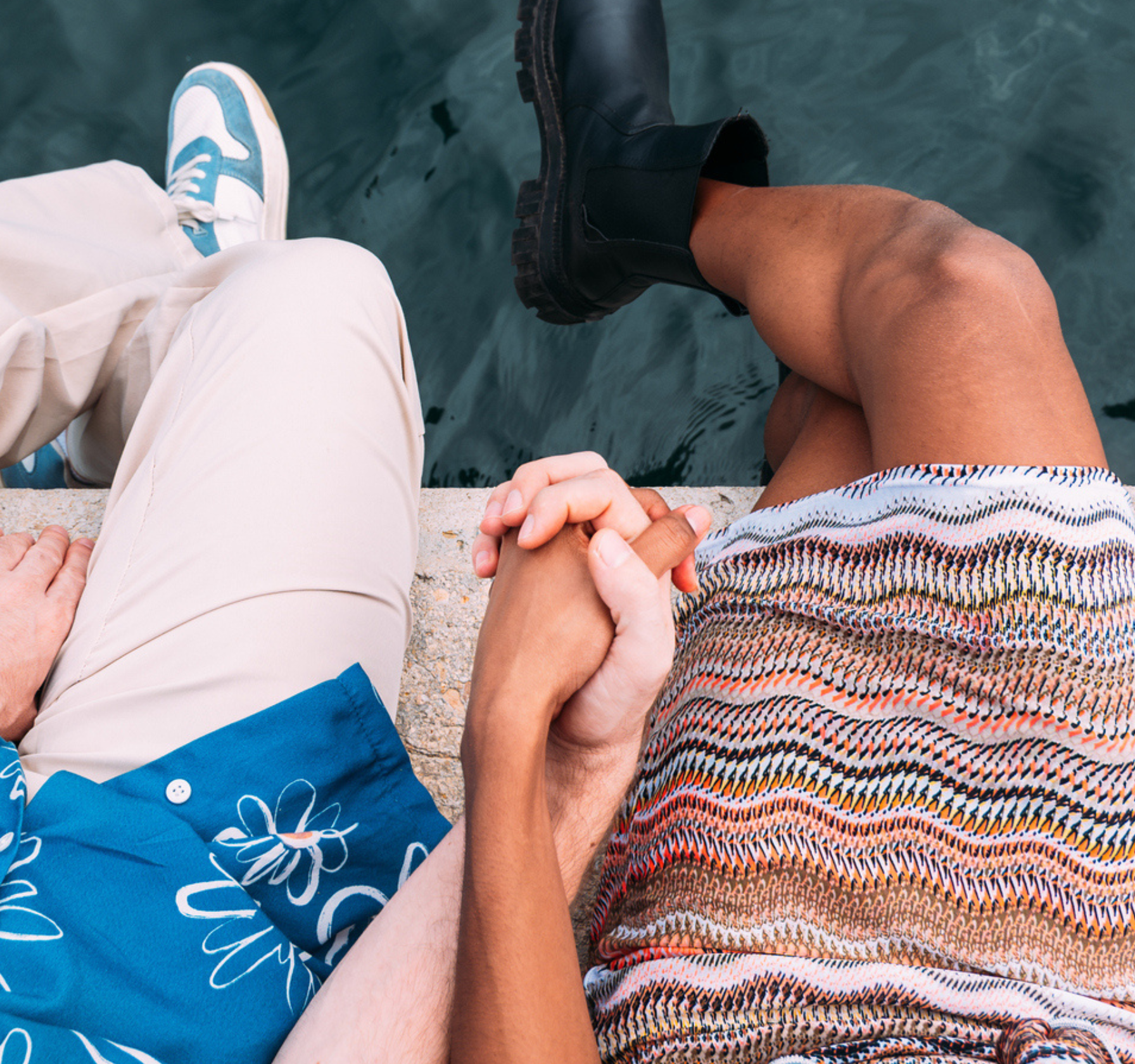 Couple holding hands sitting by the water.
